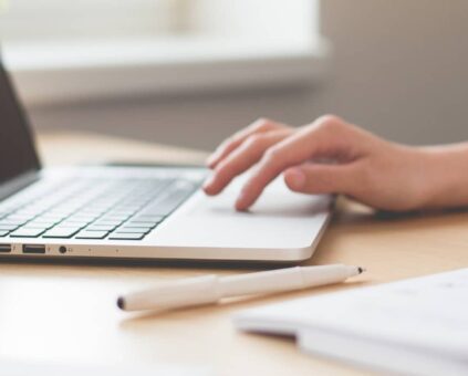 Person at laptop with pen and paper nearby