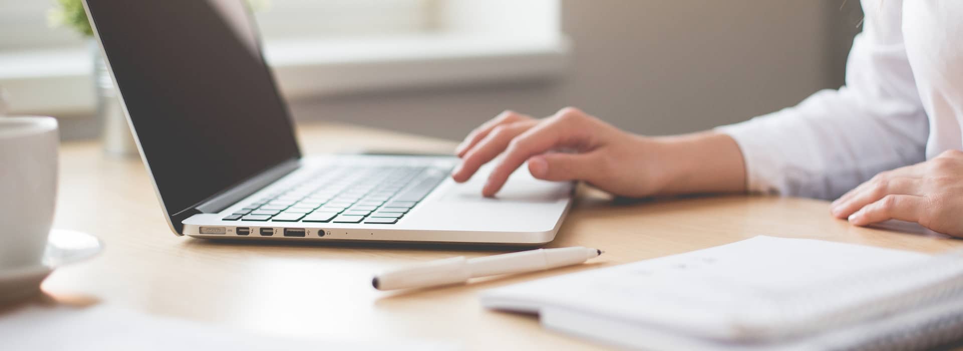 Person at laptop with pen and paper nearby