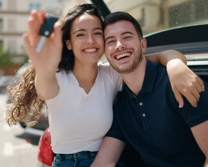 A happy Caucasian couple waving car keys from their new car in the air.