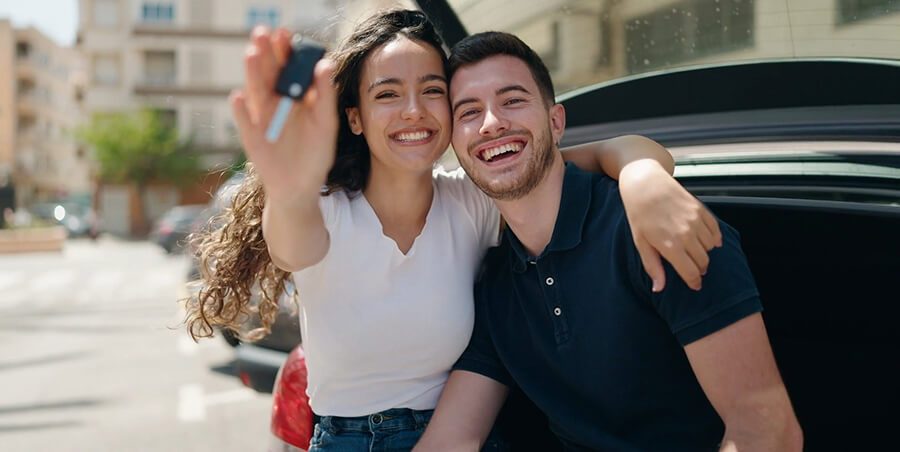 A happy Caucasian couple waving car keys from their new car in the air.
