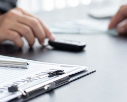 Lending specialist using calculator with car loan paperwork, representing assessment to help customers secure their Ume Loans bad credit car loan approval.