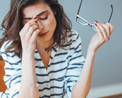 Woman experiencing financial stress holding glasses and rubbing her temples, representing the emotional burden of financial difficulties