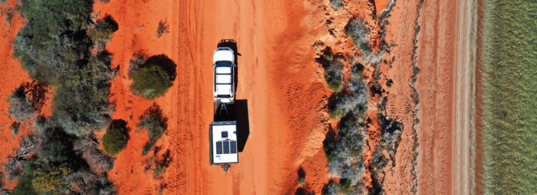 Car towing a camper trailer along a remote red‑dust road, representing how bad credit caravan and camper trailer finance can help people get back on the road.